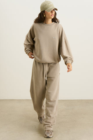 Full body front view of model posing in the relaxed fit sand french terry Varsity Crew Pullover sweatshirt with a crew neckline, dropped shoulders and a Joah Brown logo patch at the chest