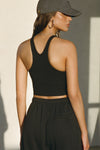 Back view of model posing in the fitted stretchy cropped black flexrib Varsity Tank Bra with a racerback silhouette
