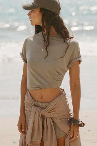 Front view of model posing on the beach in the sage grey classic cotton Vintage Tee with a crew neckline and relaxed silhouette