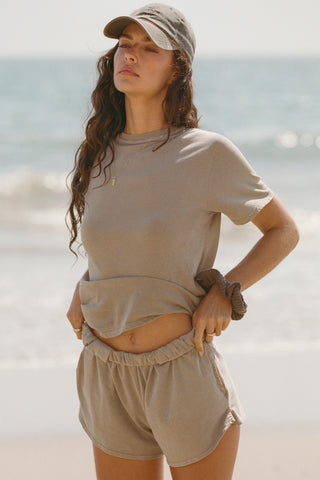 Front view of model posing on the beach in the sage grey classic cotton Vintage Tee with a crew neckline and relaxed silhouette