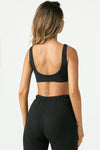 Back view of model posing in the stretchy and sculpting sueded onyx contour bra with a deep scoop back
