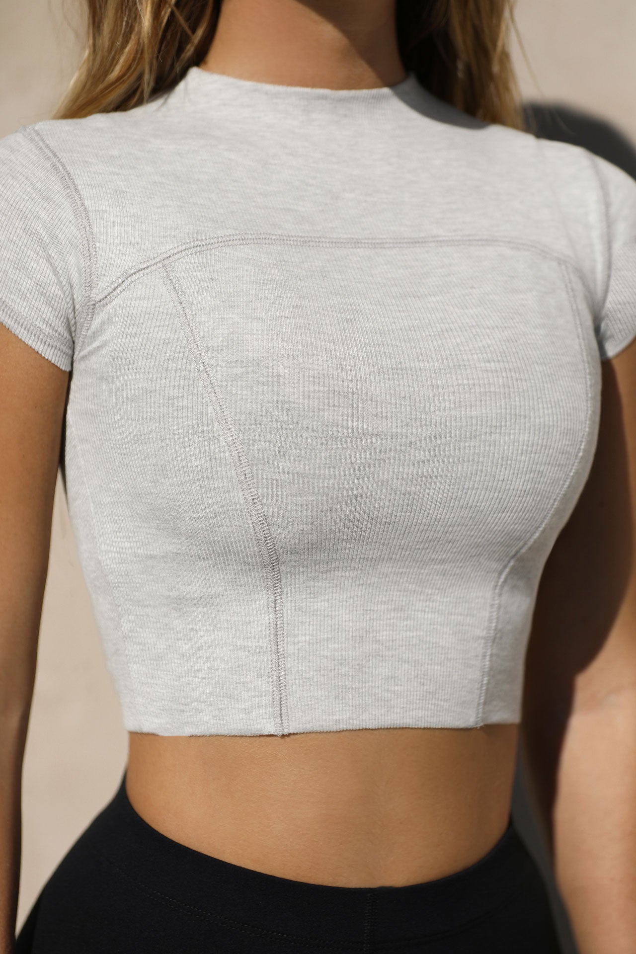 Close up detail front view of model posing in the fitted cropped pearl grey rib Contrast Stitch Crop Tee with stitched seaming, cap sleeves and a mini mock neckline