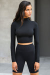 Front view of model posing in the fitted soft black modal Cropped Mock Neck Long Sleeve top with a raw cut hem