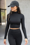 Front view of model walking outside and posing in the fitted soft black modal Cropped Mock Neck Long Sleeve top with a raw cut hem