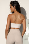 Back view of model posing in the fitted natural luxe knit Cropped Triangle Cami with triangle cup seaming along the bust, thin corded straps and a front center opening banded together with delicate knot buttons