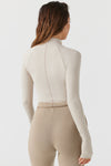 Back view of model posing in the fitted dune flexrib Stitch Mock Neck Long Sleeve top with tonal stitching on the front, a mock neckline and thumbholes in the cuffs