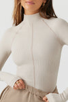 Close up front view of model posing in the fitted dune flexrib Stitch Mock Neck Long Sleeve top with tonal stitching on the front, a mock neckline and thumbholes in the cuffs