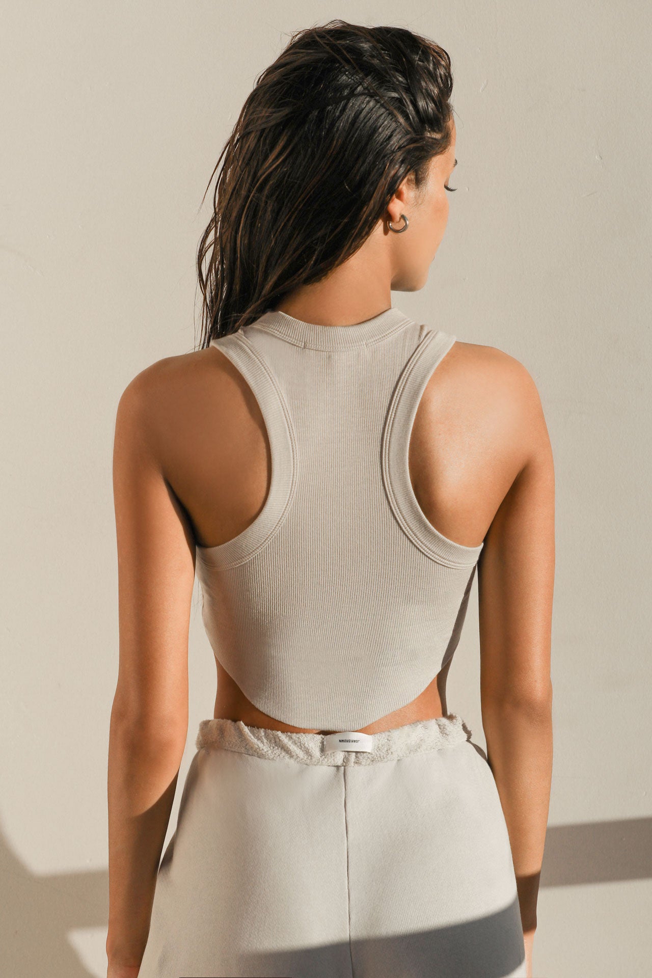 Back view of model posing in the fitted cropped dune rib Body Tank with curved hemline and a high banded crew neckline and racerback silhouette