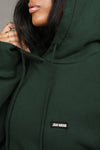 Close up detail front view of model posing in the oversized comfortable pine french terry with logo Empire Pullover Hoodie sweatshirt with a Joah Brown logo patch at the front left chest, kangaroo pocket and drawstrings at the bottom of the hood