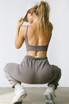Back view of model posing and crouching on the floor in the fitted stretchy mauve flexrib Low Back Crop Cami with a deep scoop back and skinny straps