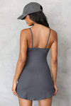 Back view of model posing in the form fitting stretchy smoke rib mini Slip Dress with thin straps, a u neckline and a tiny side slit at the hem