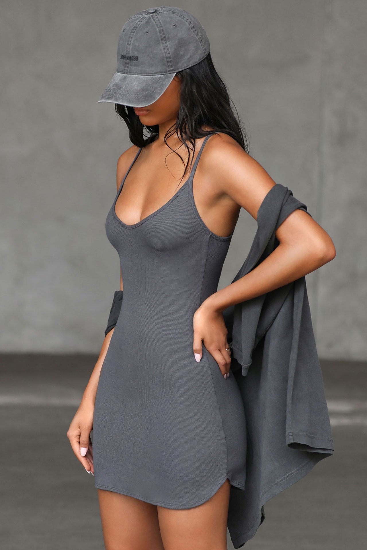 Side view of model posing in the form fitting stretchy smoke rib mini Slip Dress with thin straps, a u neckline and a tiny side slit at the hem