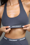 Close up detail front view of model posing in the fitted and stretchy sueded navy The Sports Bra with a scoop neckline and an elastic under band printed with the Joah Brown logo