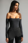 Front view of model posing in the form fitting sueded onyx Off The Shoulder Long Sleeve Top in a cold shoulder design with ultra thin corded straps, attached sleeves and a straight neckline